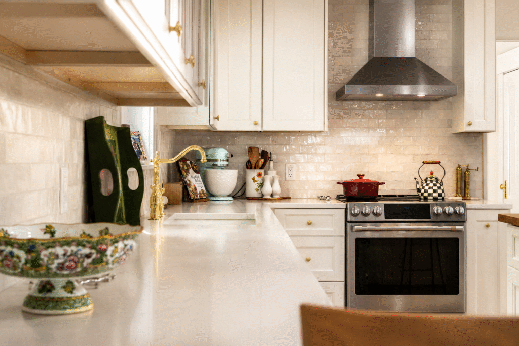 Bright kitchen with white cabinets, marble countertop, and a stainless steel range hood above a gas stove with a red pot.